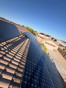 1000265286 - Desert Sands Contracting Residential roof with dark solar panels installed on a sloped terracotta tile roof under a clear blue sky.