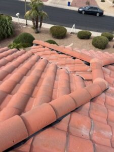 AIMG_2337 - Desert Sands Contracting Close-up of a clay tile roof showing a cracked ridge with several tiles displaced or damaged, viewed from above.