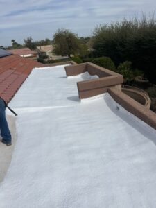 IMG_2318 - Desert Sands Contracting Person on a flat white-coated roof applying waterproof coating; brown parapet walls and trees in the background.