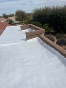 IMG_2319 - Desert Sands Contracting Top-down view of a white flat roof with brown parapet walls in a suburban neighborhood with trees in the background.