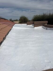 IMG_2322 - Desert Sands Contracting Flat roof coated in white reflective sealant with red clay tile edging on the left and low parapet walls on the right under a blue sky.