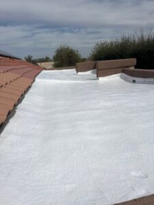 IMG_2323 1 - Desert Sands Contracting Flat white-coated rooftop with terracotta tiles along the left edge and brown parapet walls under a cloudy blue sky.