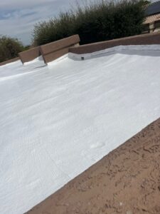 IMG_2324 - Desert Sands Contracting Flat roof coated in white reflective material with brown parapet walls and shrubs in the background.