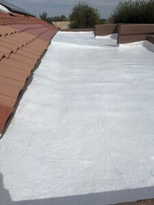 IMG_2325 - Desert Sands Contracting Flat roof coated in white reflective sealant, with terracotta tiles along the left edge and trees in the distance.