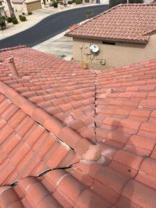 IMG_2328 - Desert Sands Contracting From above, cracked red clay tile roof along the ridge with a split seam; neighboring stucco house with a satellite dish and utility meters visible.