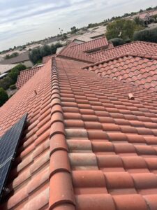 IMG_2334 - Desert Sands Contracting Red clay tile roof with a solar panel on the left, overlooking a suburban neighborhood with more tile roofs and palm trees in the distance.