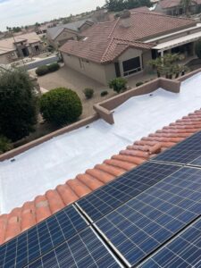 IMG_2335 - Desert Sands Contracting Solar panels installed on a red tile roof with white flat roofing and beige houses in the background.