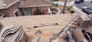 PHOTO-2025-01-30-06-50-05 - Desert Sands Contracting Rooftop under construction with loose clay tiles, a hammer and debris on the roof, overlooking a suburban street.