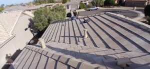 PHOTO-2025-02-01-15-52-34 - Desert Sands Contracting Aerial view of a tile roof under repair with two workers on top and a suburban street in the background.