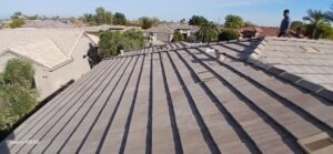 PHOTO-2025-02-01-15-52-35 - Desert Sands Contracting Wide view of a suburban neighborhood with brown tile roofs; two workers on a sloped roof under a clear sky.