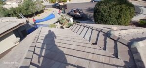 PHOTO-2025-02-01-15-52-42_2 - Desert Sands Contracting Shadow of a person on a tan tiled roof overlooking a street where workers lay out a blue tarp and park trucks nearby.