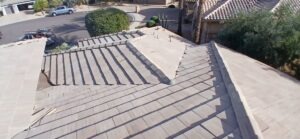 PHOTO-2025-02-01-15-52-45 - Desert Sands Contracting Aerial view of a light-gray tiled roof with intersecting ridges in a suburban neighborhood.