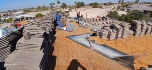 PHOTO-2025-02-01-15-52-47 - Desert Sands Contracting Workers install concrete roof tiles on a house under construction, with piles of tiles and metal flashing on a plywood roof
