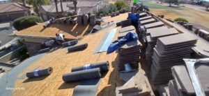 PHOTO-2025-02-01-15-52-50 - Desert Sands Contracting Overhead view of a roof underlayment project with plywood decking, tile stacks, rolls of roofing felt, and workers in the distance.