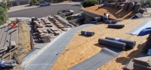 PHOTO-2025-02-01-15-52-50_2 - Desert Sands Contracting Rooftop under construction with rolled roofing membranes, plywood sheathing, and stacked lumber on a suburban house